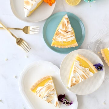 four dessert plates filled with a slice of lemon tart with two forks.