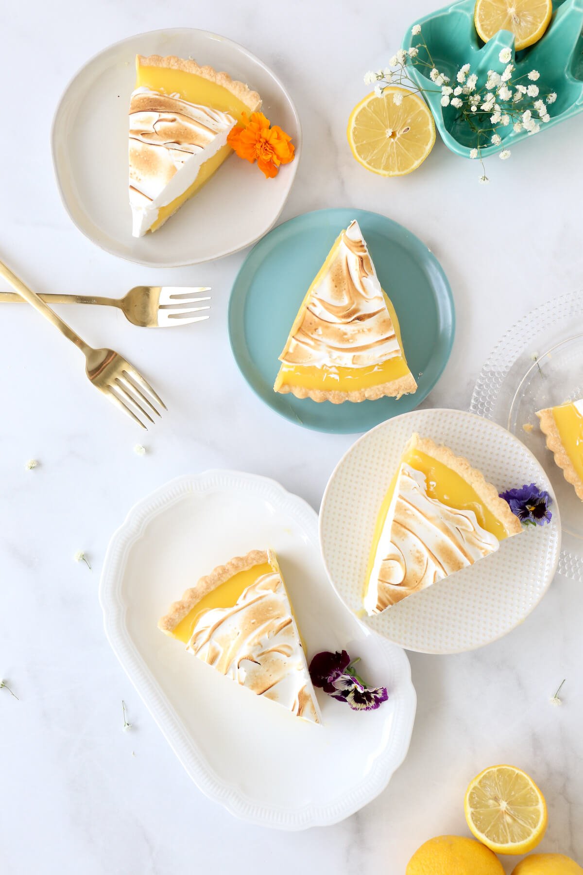 four dessert plates filled with a slice of lemon tart with two forks.