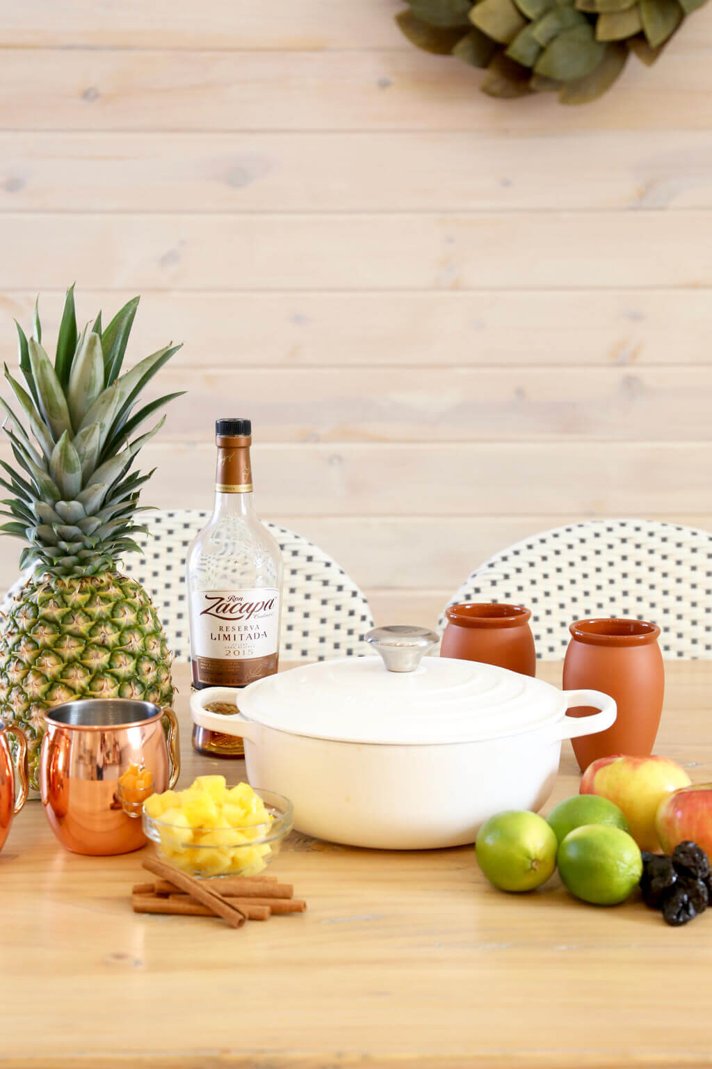 a pot, chopped pineapple, limes, apples, prunes, rum and copper mugs 