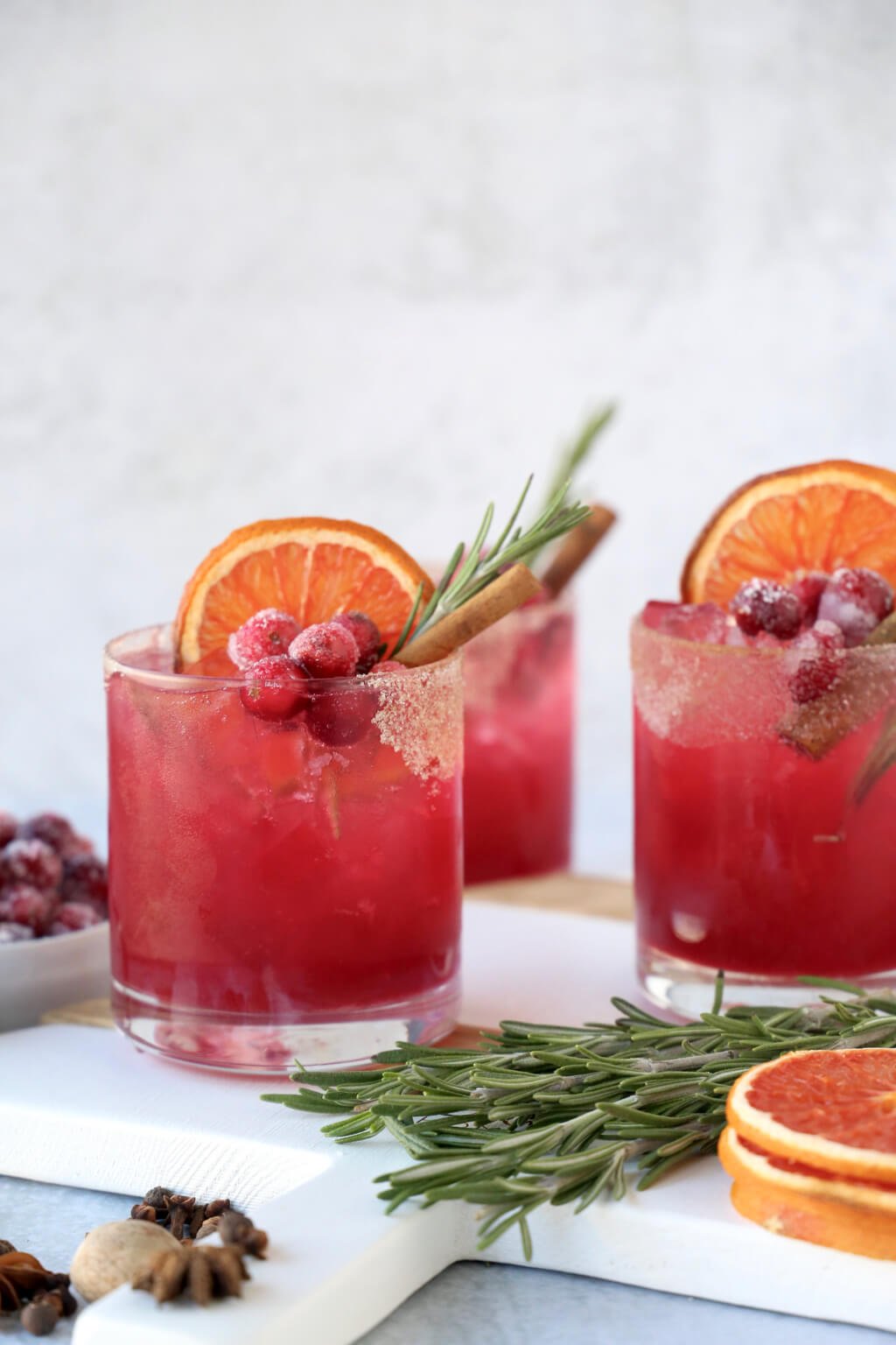 three glasses of a christmas cocktail with rosemary, cinnamon and dried grapefruit 