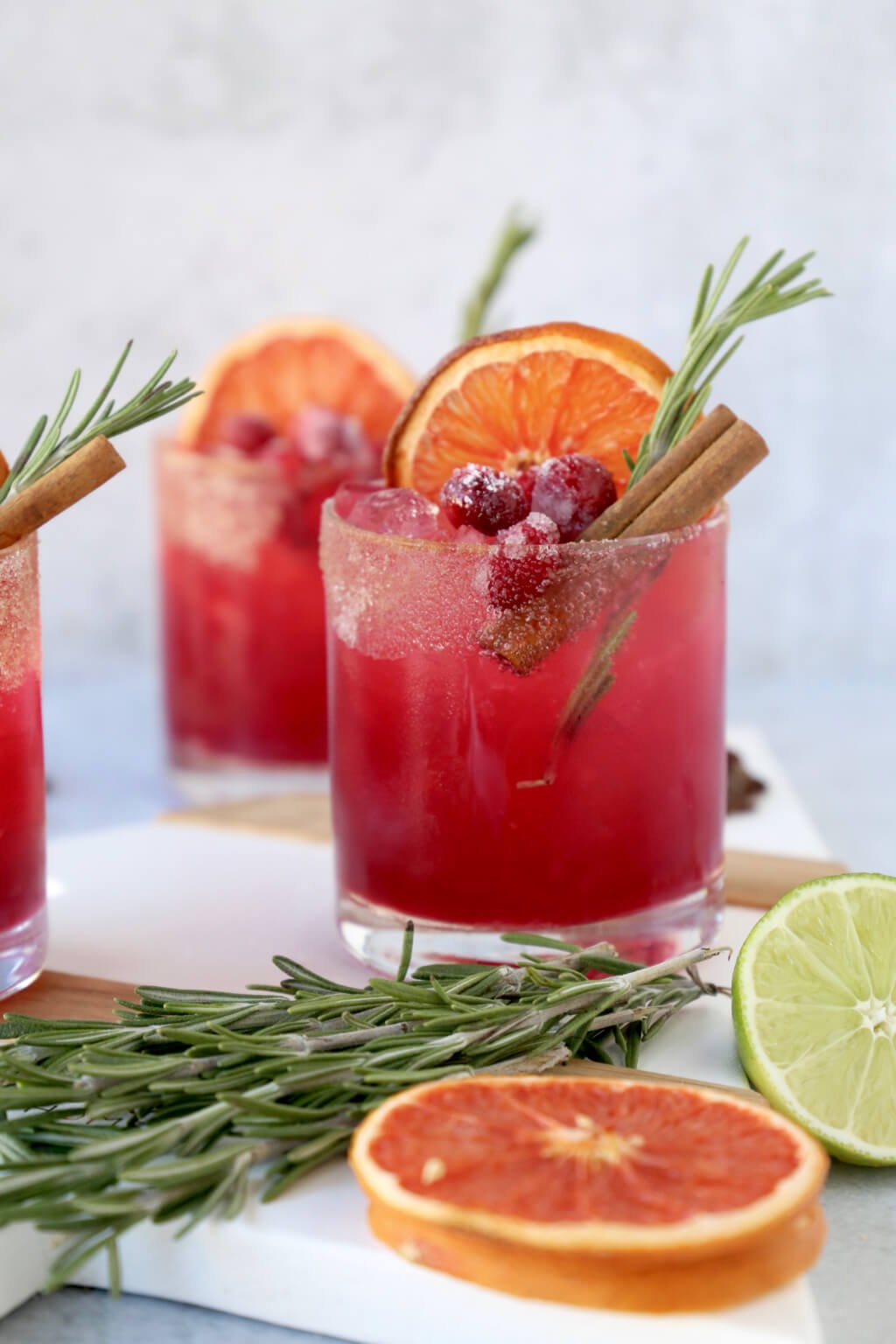 three glasses of a christmas cocktail with rosemary, cinnamon and dried grapefruit