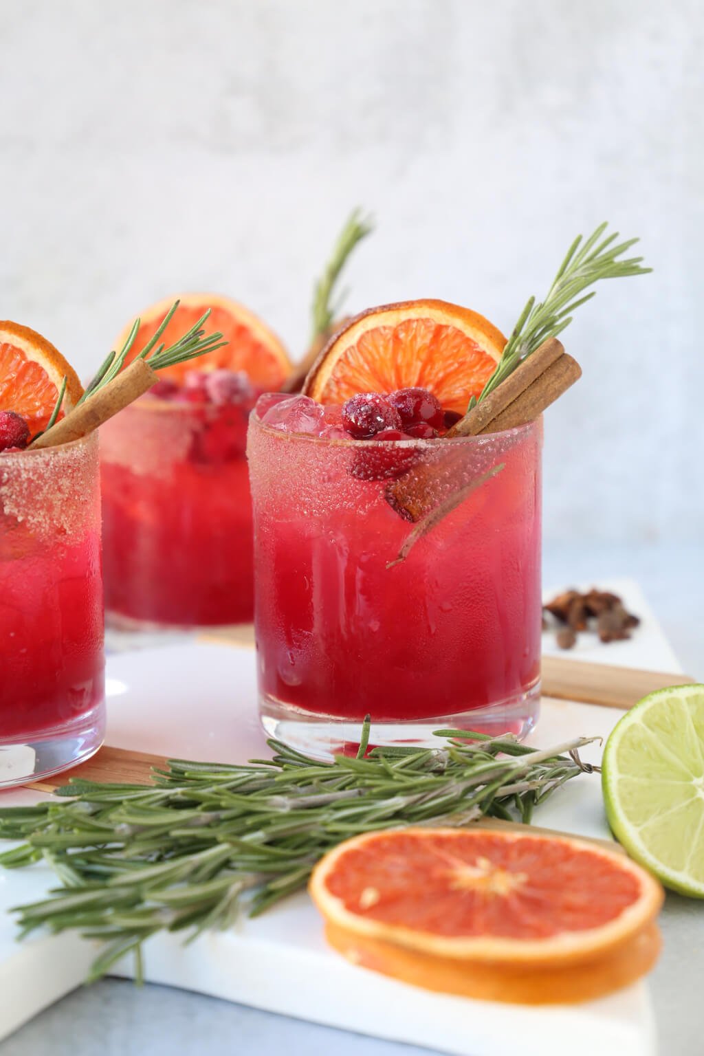 three glasses of a christmas cocktail with rosemary, cinnamon and dried grapefruit