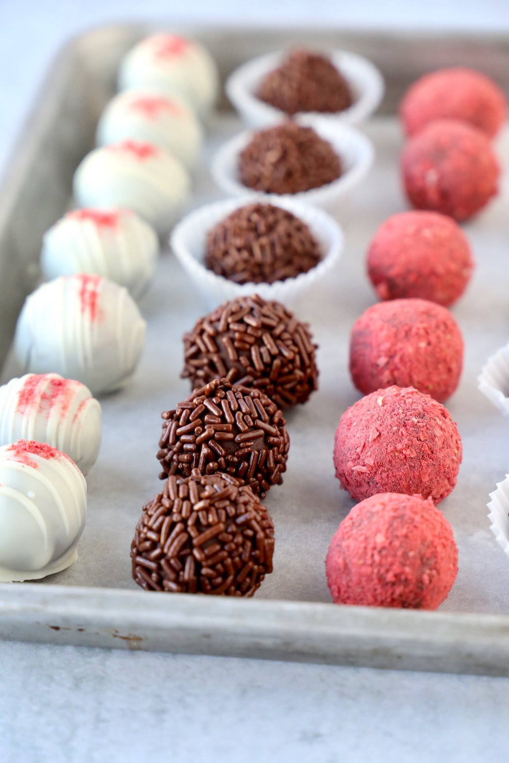Three rows of truffles dipped in white chocolate, chocolate sprinkles and freeze dried raspberries 