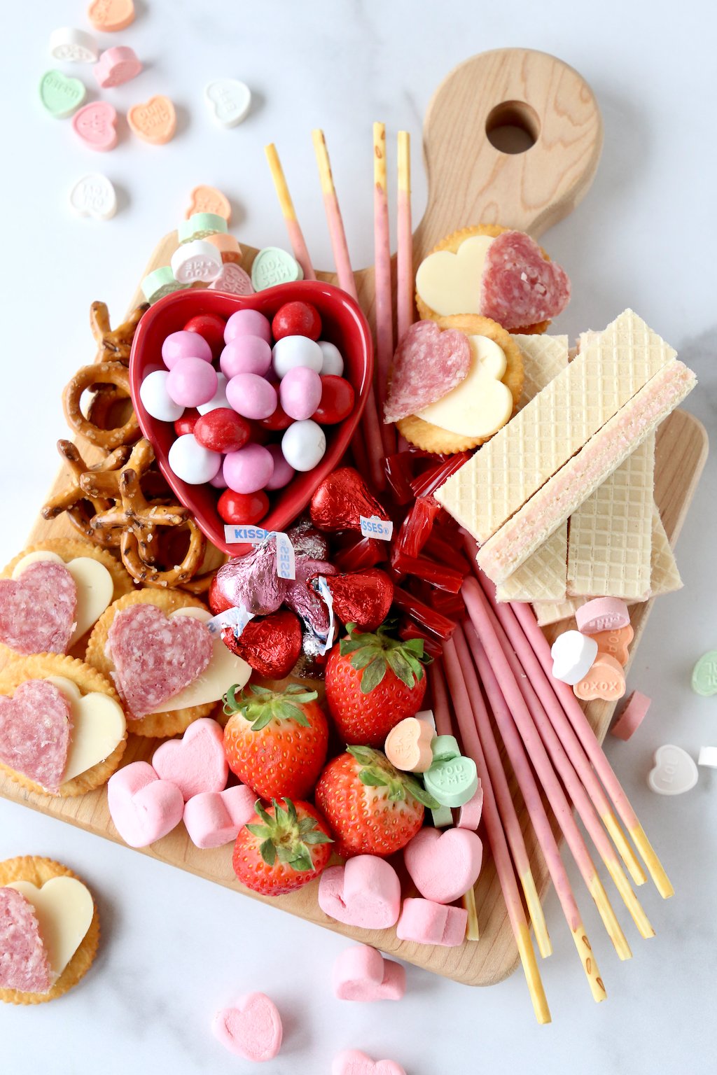 a wood cutting board filling with chocolate, marshmallows, strawberries, wafer cookies and salami and cheese crackers