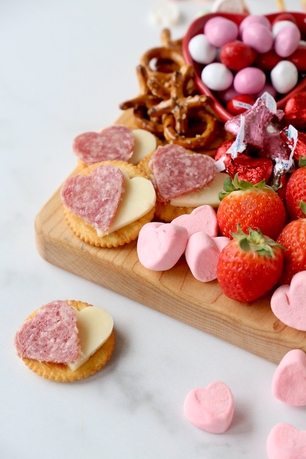 heart shaped salami and cheese on crackers placed on a valentine's snack board 