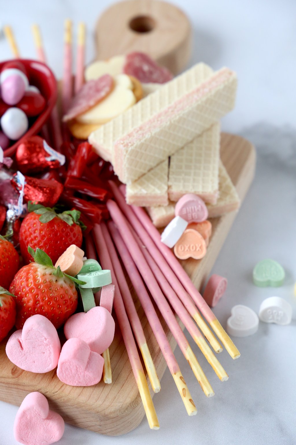 strawberry pokey sticks, strawberry wafer cookies, conversation hearts, chocolate and strawberries stacked on a wood board 