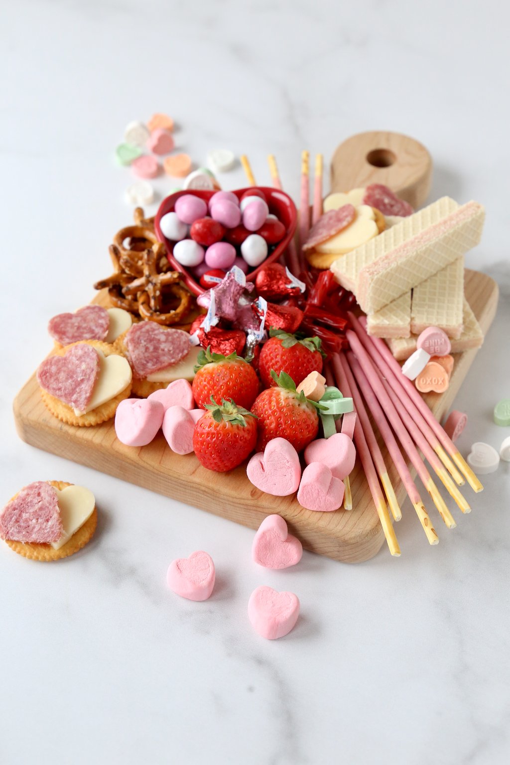 a wood cutting board filling with chocolate, marshmallows, strawberries, wafer cookies and salami and cheese crackers 