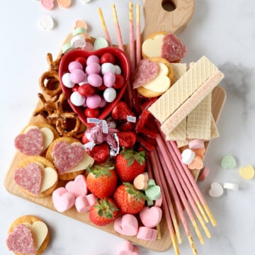 a wood cutting board filling with chocolate, marshmallows, strawberries, wafer cookies and salami and cheese crackers