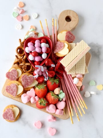 a wood cutting board filling with chocolate, marshmallows, strawberries, wafer cookies and salami and cheese crackers