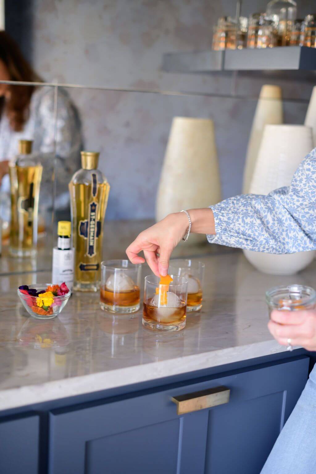 placing an orange peel in a glass filled with bourbon, bitters and elderflower