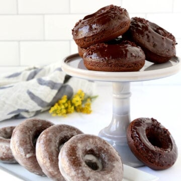 a cake stand stacked with chocolate donuts and a platter of glazed donuts next to it