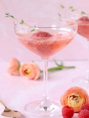 a glass of champagne with a scoop of raspberry sorbet and a sprig of thyme