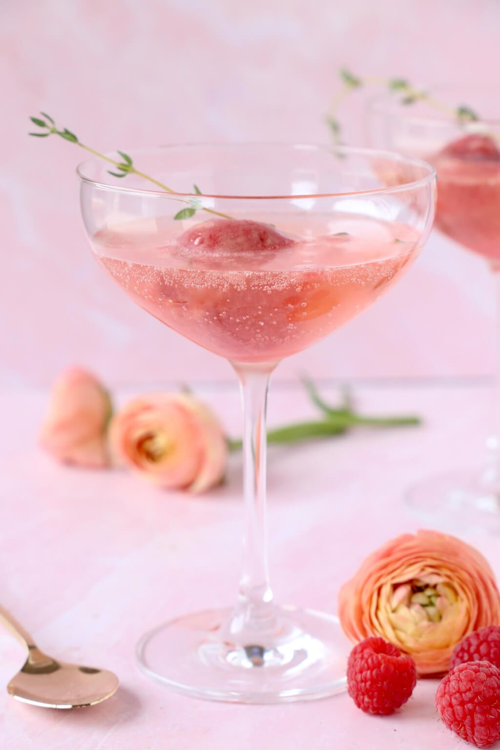 a glass of champagne with a scoop of raspberry sorbet and a sprig of thyme