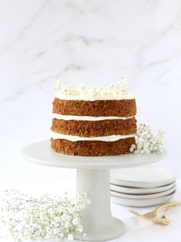 three layers of carrot cake on a gray cake stand with babies breath garnishing the cake