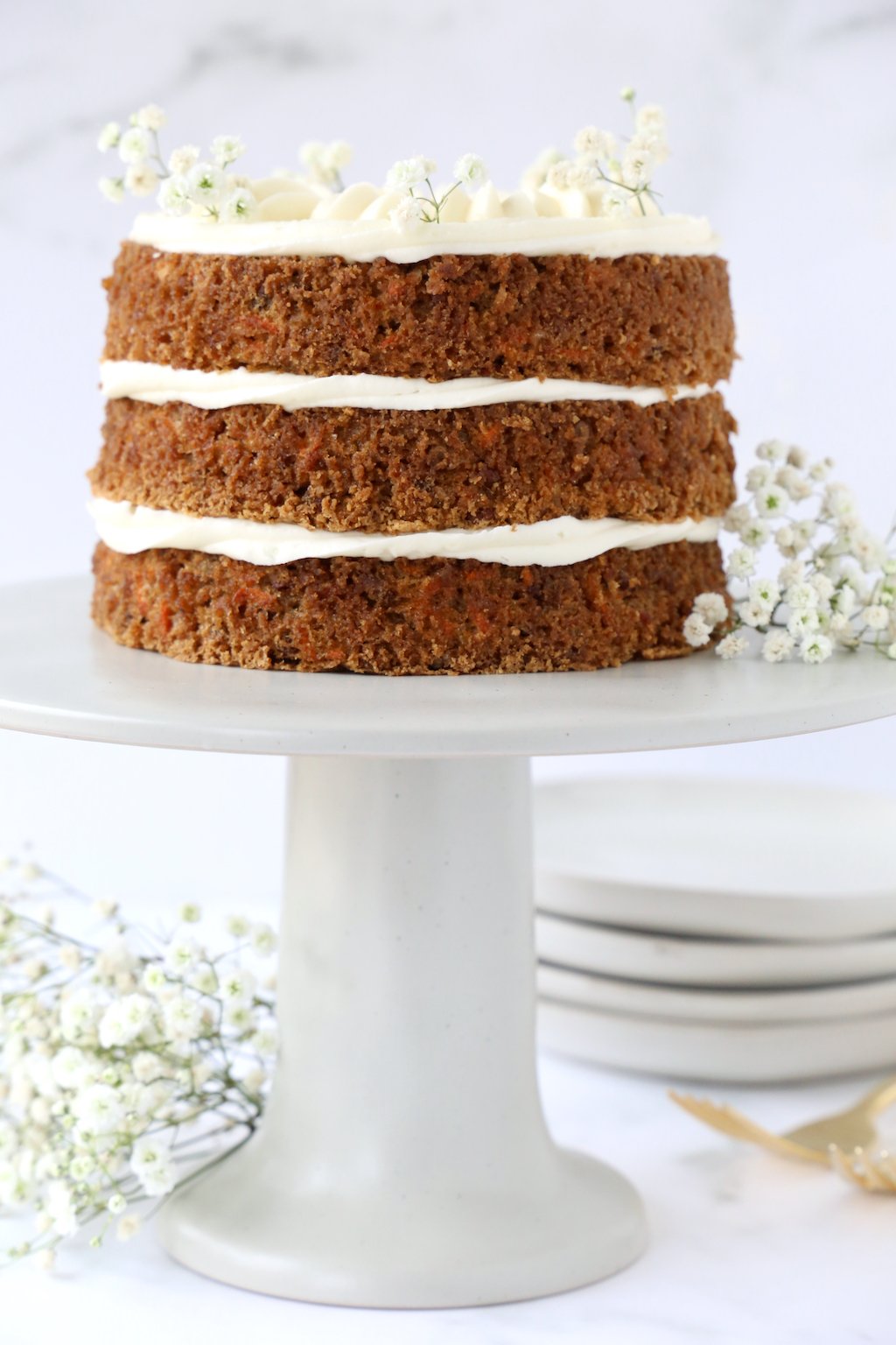 three layers of carrot cake on a gray cake stand with babies breath garnishing the cake