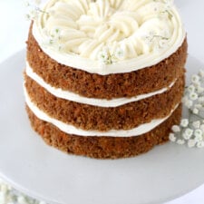 Three layers of carrot cake and cream cheese frosting on a gray cake stand