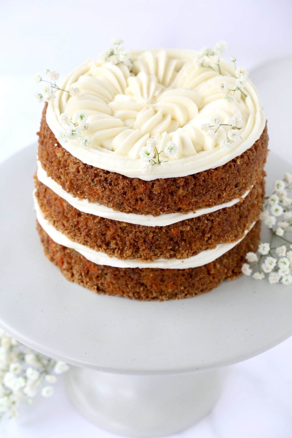 Three layers of carrot cake and cream cheese frosting on a gray cake stand