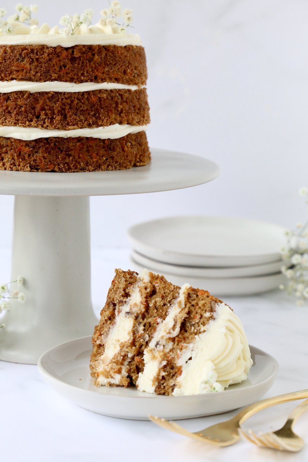 Three layers of carrot cake on a cake stand with a slice of carrot cake in front of it