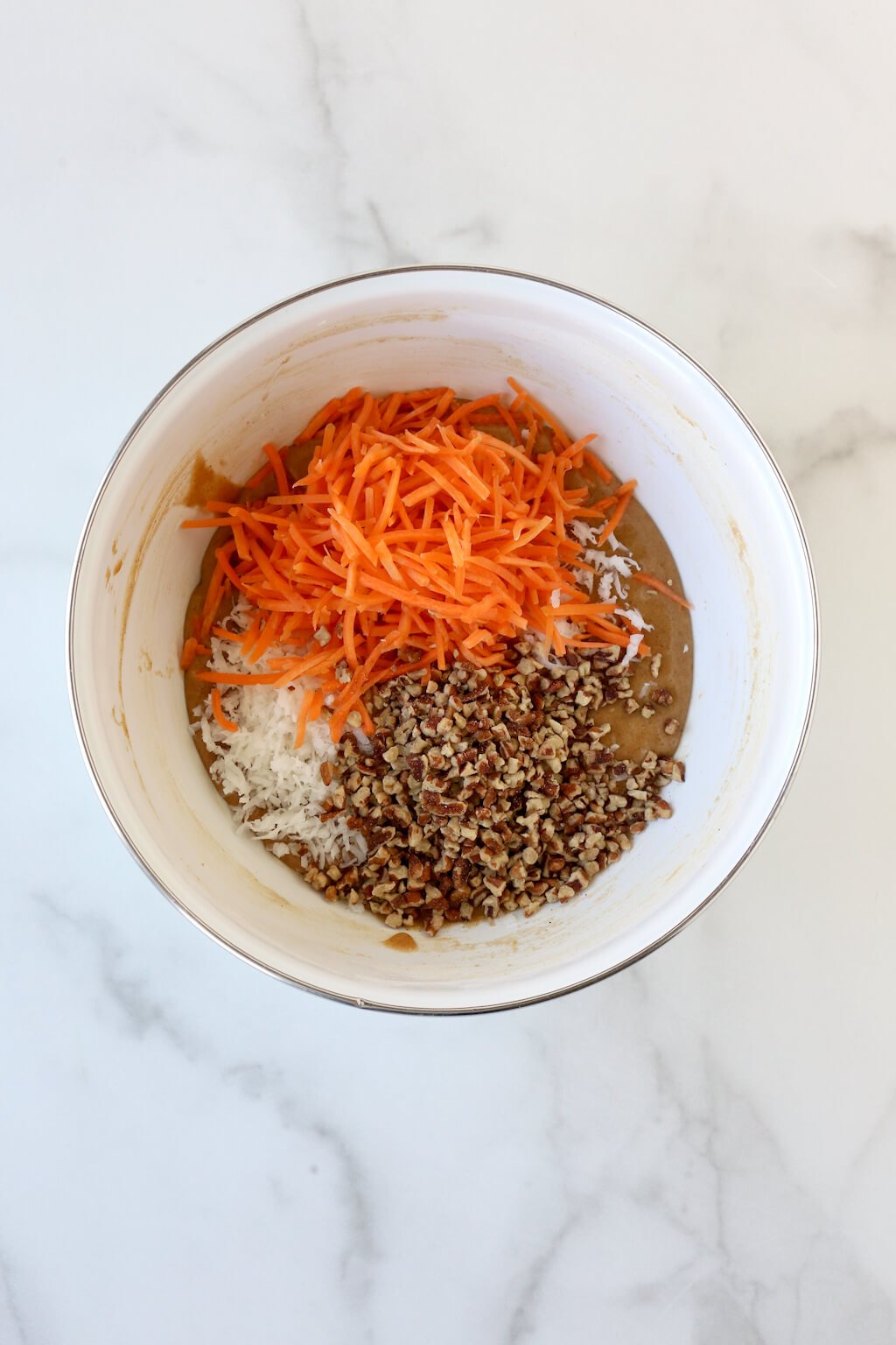 a bowl of cake batter topped with shredded carrots, pecans and coconut