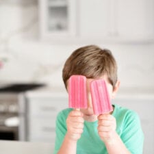 two strawberry banana popsicles held up by a little boy