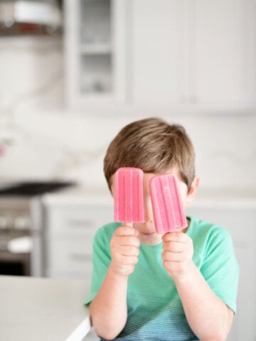 two strawberry banana popsicles held up by a little boy