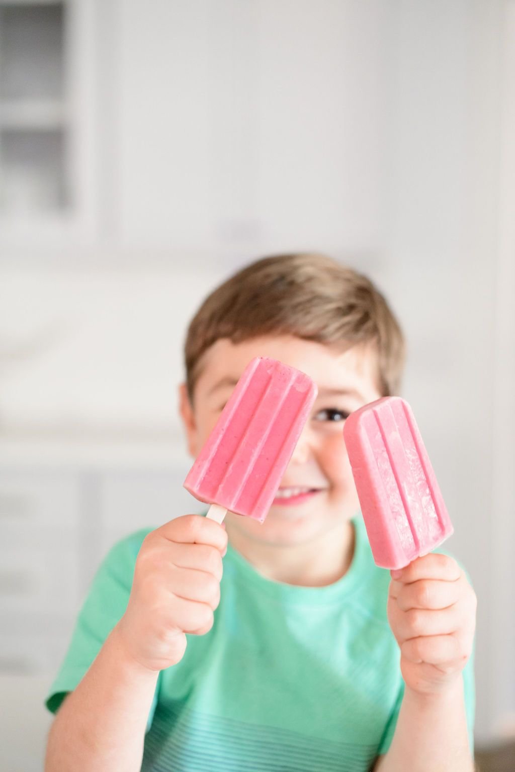 two strawberry banana popsicles held up by a little boy