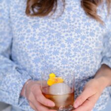 a glass of bourbon, bitters and st. germain in from of a blue floral shirt