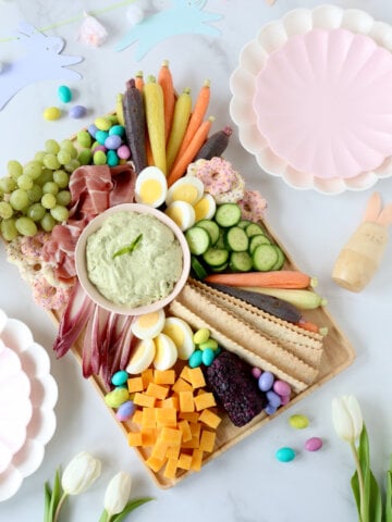 a platter of meats, cheeses, veggies and chocolate in the center of easter decorations