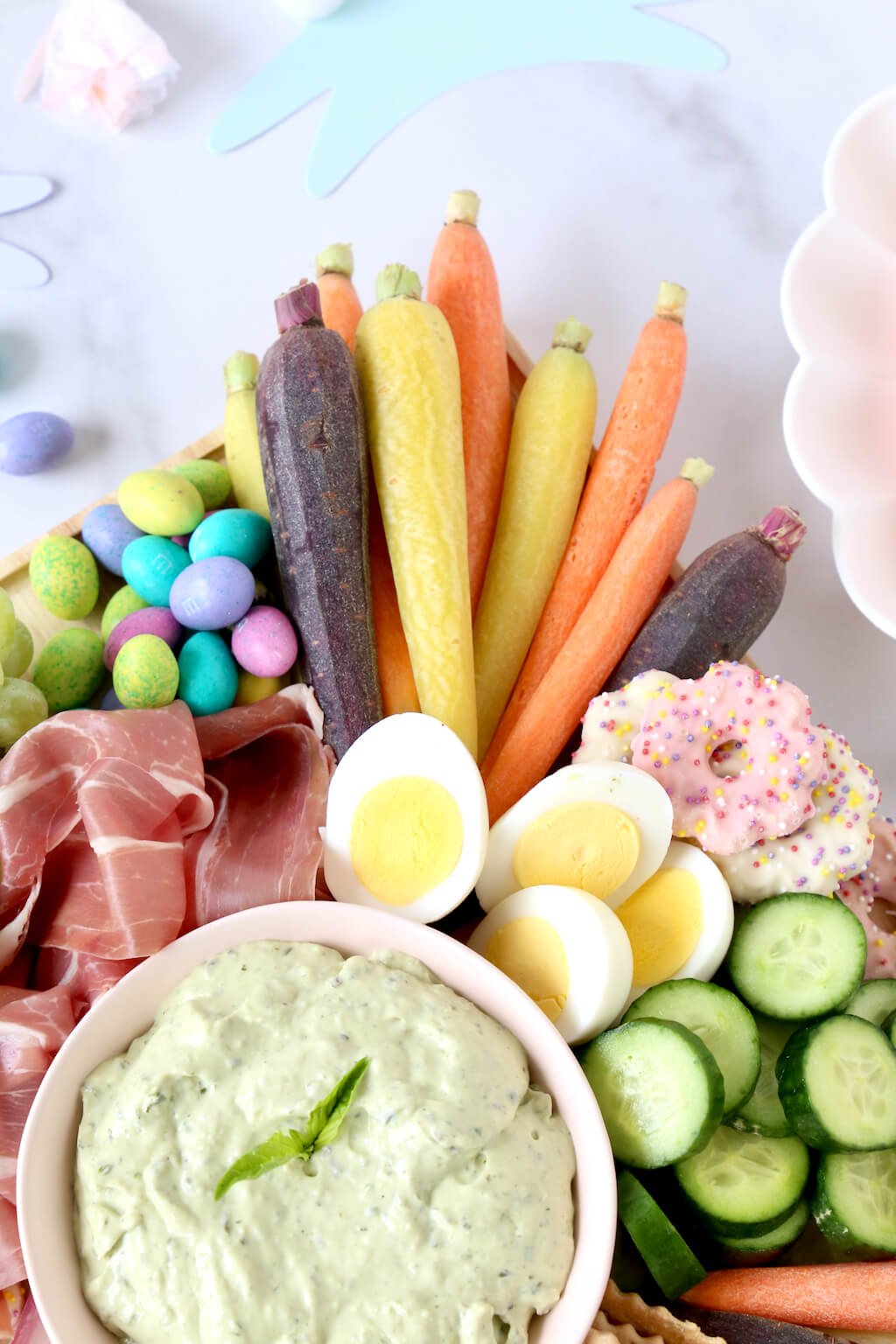 green dip, carrots, boiled eggs, cucumbers and prosciutto on a board 