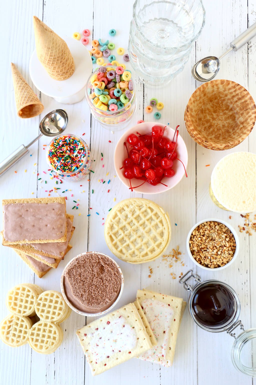 a spread of ice cream, waffles, pop tarts, cherries, cereal, ice cream cones and chocolate sauce