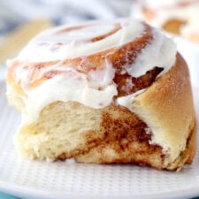 a close up of one cream cheese glazed cinnamon roll on sitting on two plates.