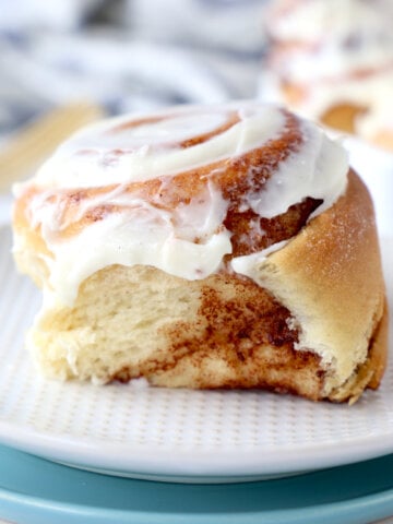 a close up of one cream cheese glazed cinnamon roll on sitting on two plates.