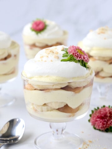 a glass trifle dish filled with vanilla pudding, bananas, wafer cookies and fresh whipped cream with pink flowers.
