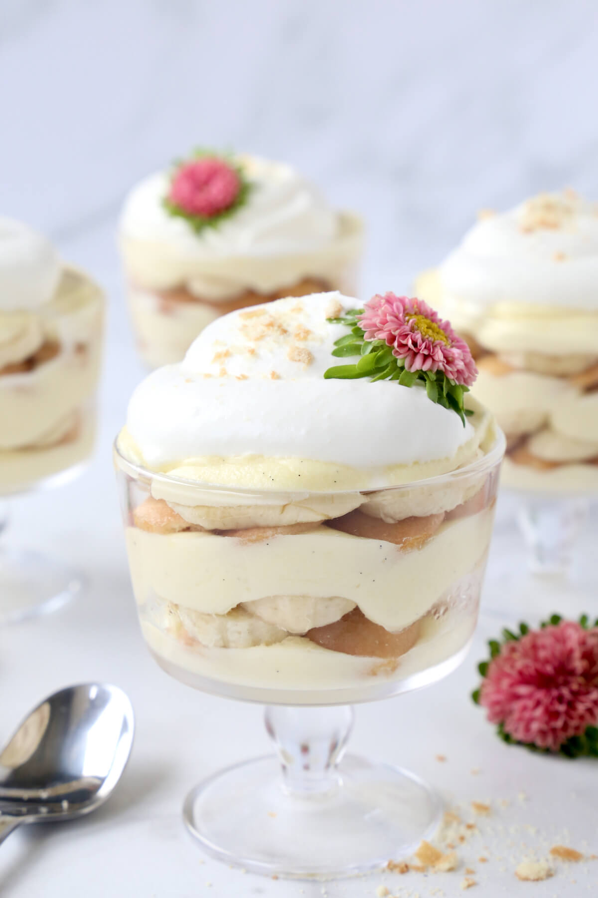 a glass trifle dish filled with vanilla pudding, bananas, wafer cookies and fresh whipped cream with pink flowers. 
