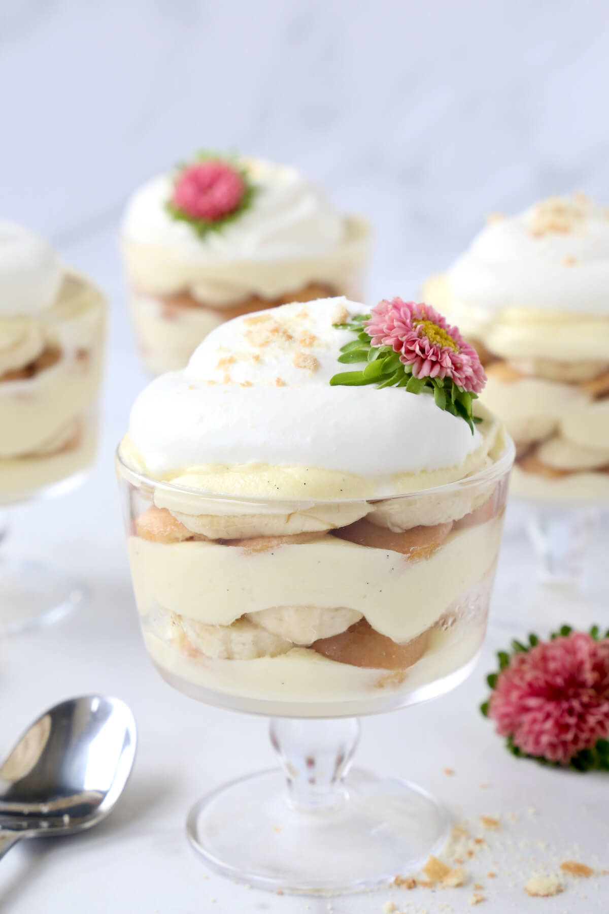 a glass trifle dish filled with vanilla pudding, bananas, wafer cookies and fresh whipped cream with pink flowers.