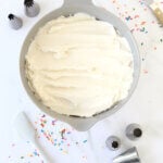 a bowl of white frosting surrounded by sprinkles, piping tips and spatulas.