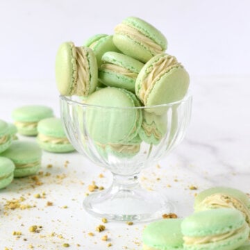 a clear glass filled with green cookies and crushed pistachios