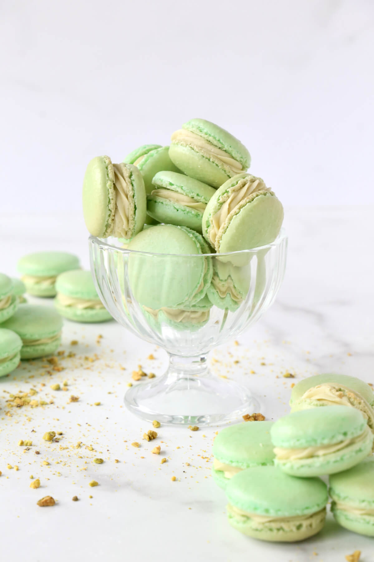 a clear glass filled with green cookies and crushed pistachios 