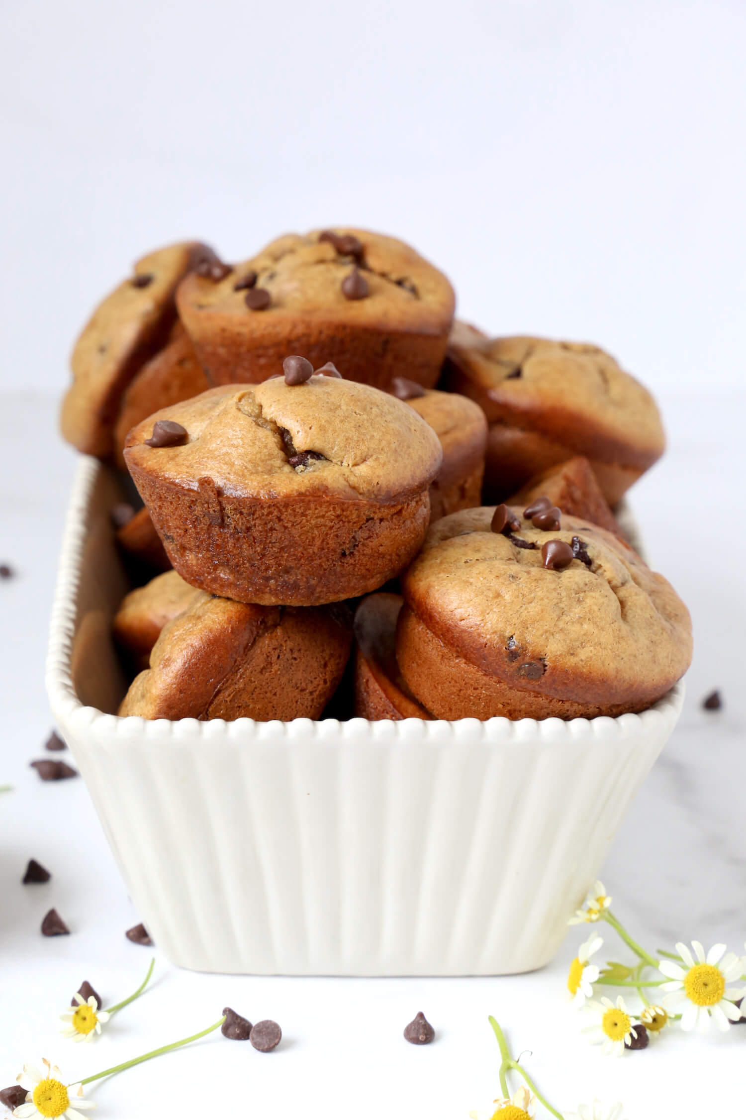 A pile of muffins in a white loaf dish with chocolate chips scattered.  