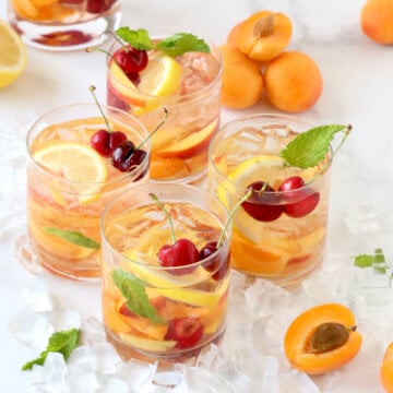 Four glasses filled with rose wine, cherries, lemons, nectarines and apricots.