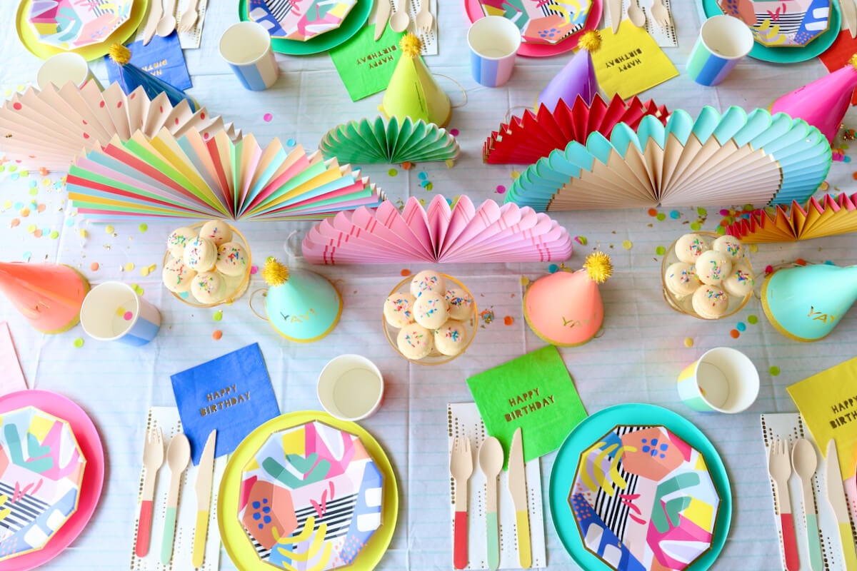 a colorful table full of paper plates, napkins, party hats, confetti and french macarons.  