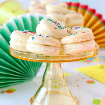 A mini cakestand stacked with white french macarons on a colorful decorated table.