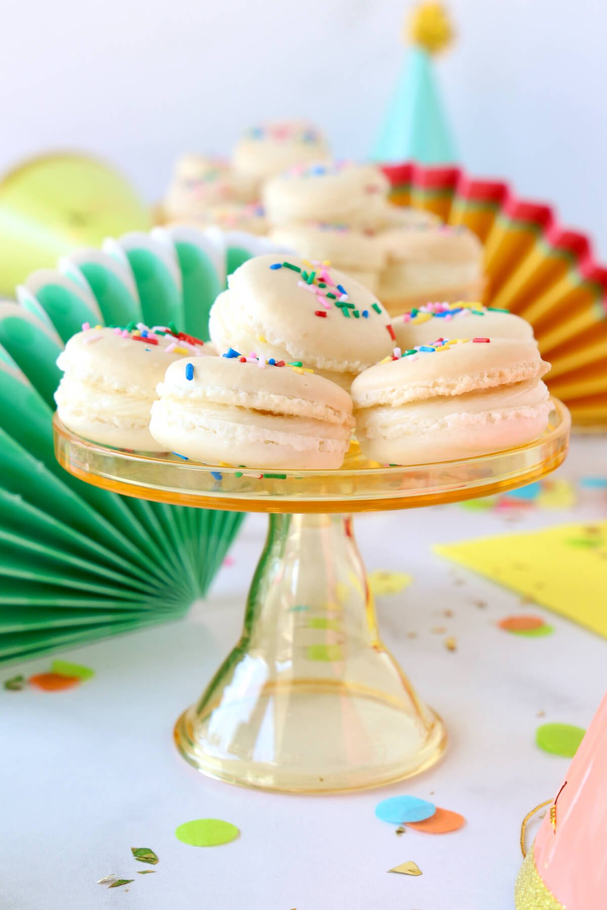 A mini cakestand stacked with white french macarons on a colorful decorated table.  