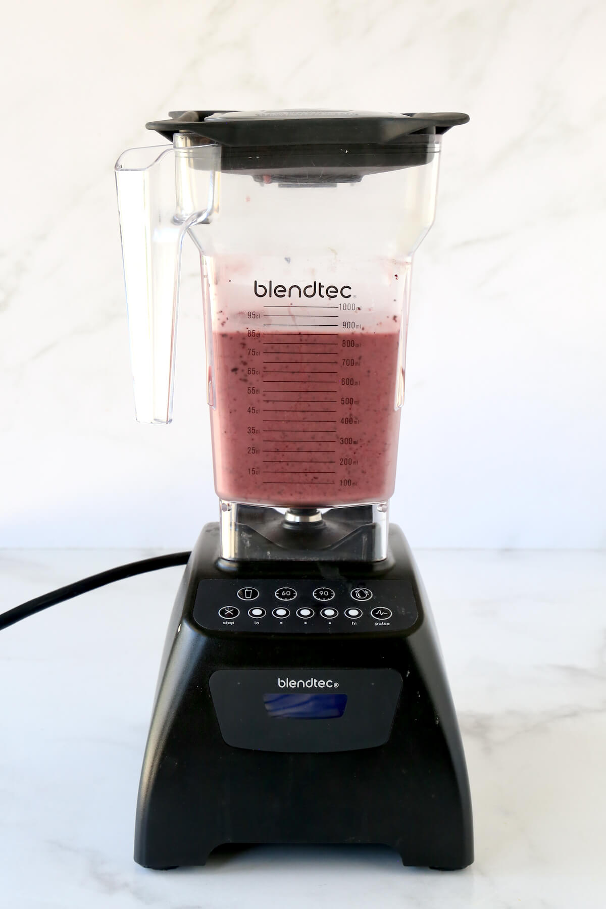 A blendtec mixer with the blueberry smoothie mixture blended up.