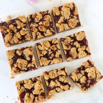 A square cut into nine pieces of peanut butter and jelly bars with flowers sprinkled around.
