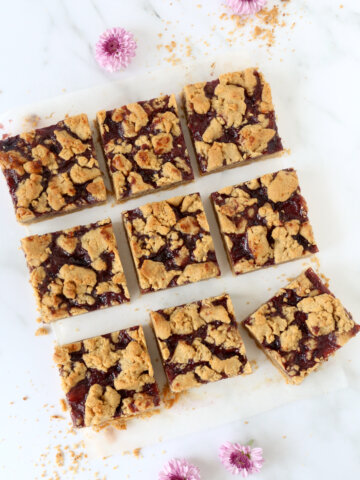 A square cut into nine pieces of peanut butter and jelly bars with flowers sprinkled around.