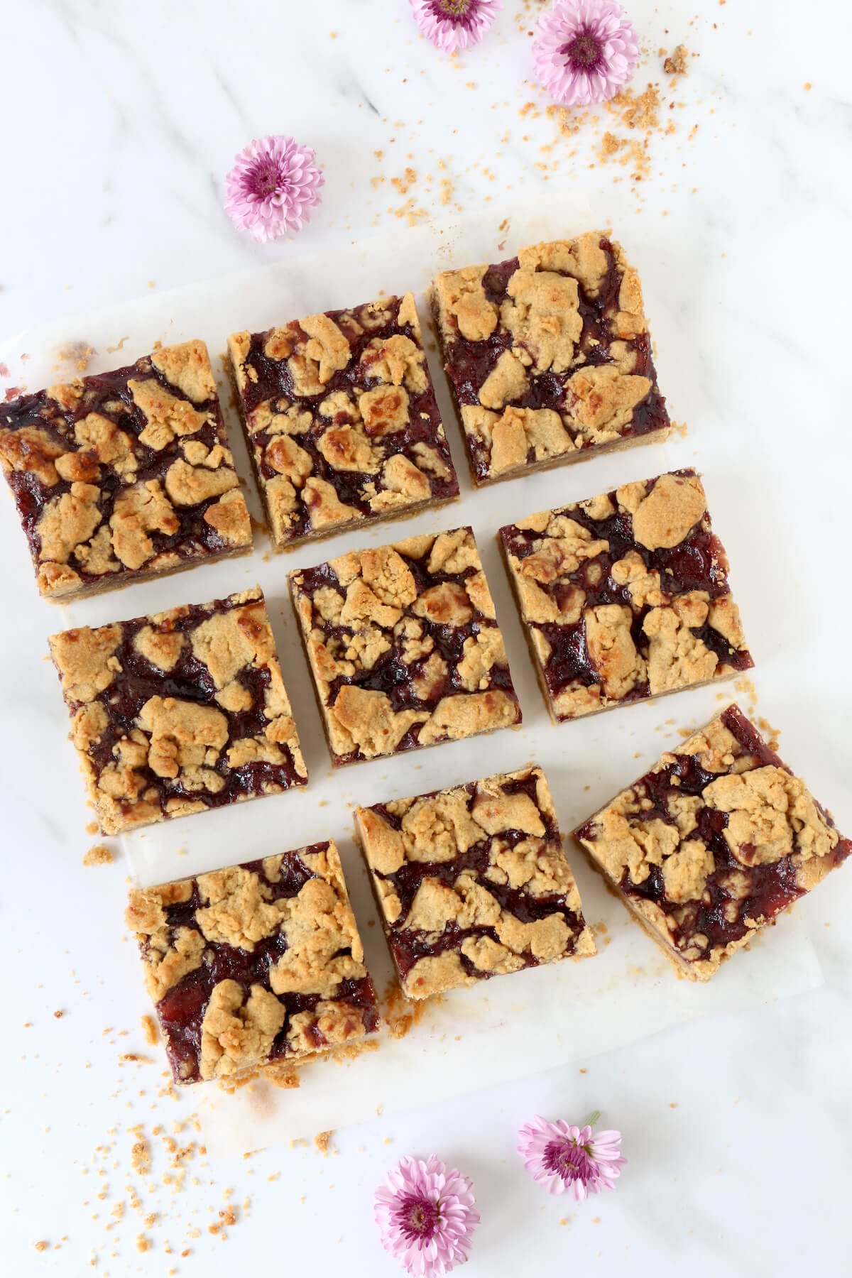 A square cut into nine pieces of peanut butter and jelly bars with flowers sprinkled around.