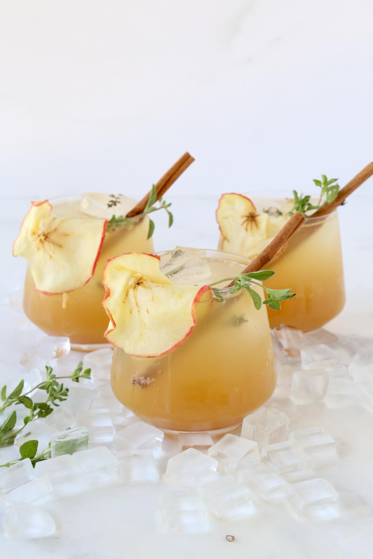 Three glasses filled with bourbon, apple cider, simple syrup and sparkling water and garnished with a cinnamon stick and apples slice.