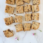 Square blondies laying on parchment paper with fresh flowers.