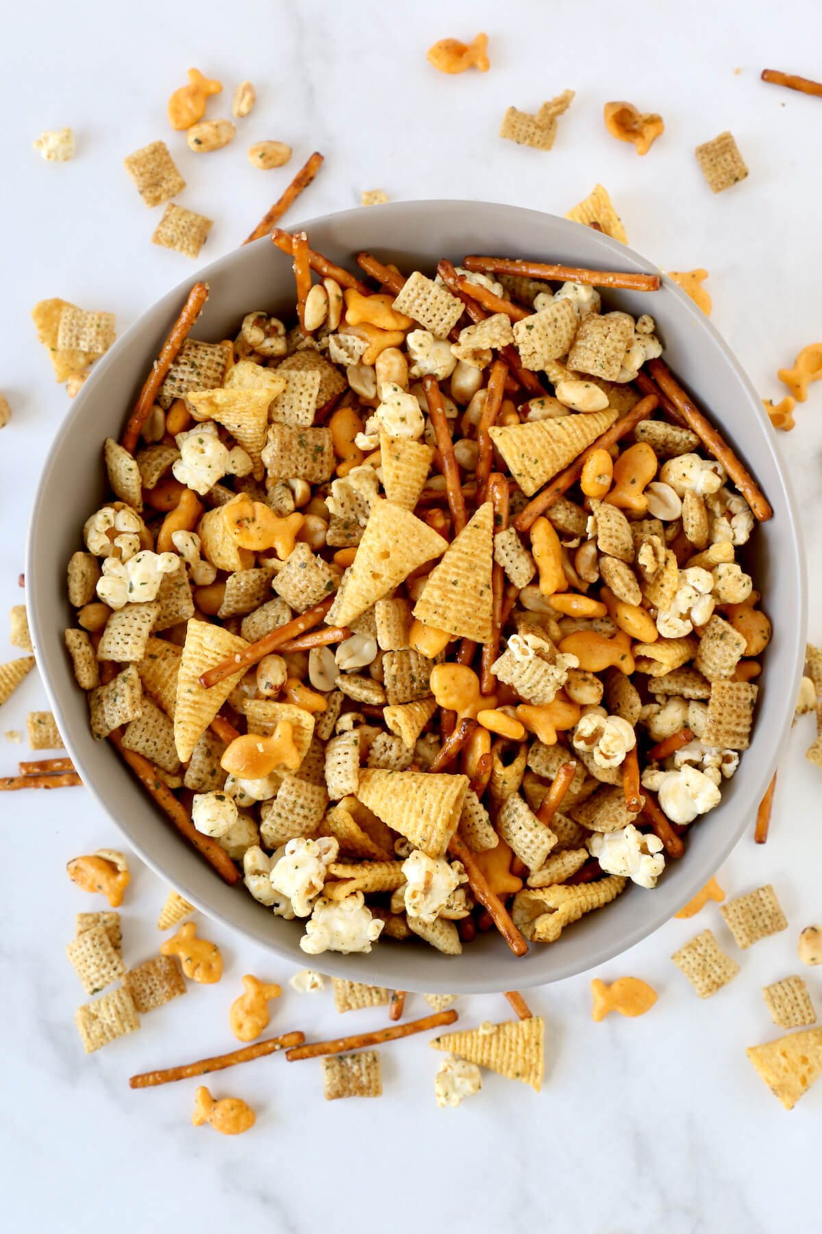 A gray bowl filled with seasoned pretzels, bugels, gold fish, popcorn, peanuts and chex cereal.